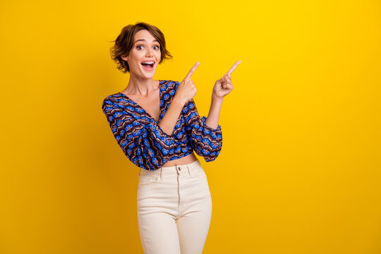 Photo of young amazed girl brown bob hair wearing blouse pointing fingers empty space right side isolated on yellow color background