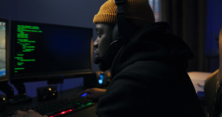 Focused operative performs a cyber task in a dim room. The man types rapidly, hacking through...