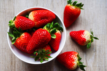 Large ripe strawberries in a white plate next to strawberry berries on a gray wooden table