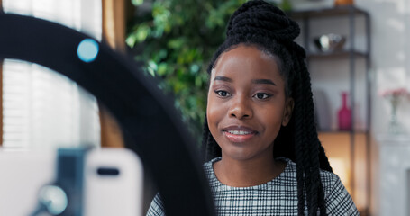 Close-up of young female influencer working online, creating social media content, recording beauty video through ring light with phone tripod, sharing tips for teenage girls.