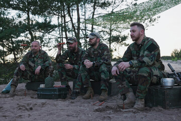 Military men in moro uniforms relax after their afternoon shift at the base, sitting on crates,...