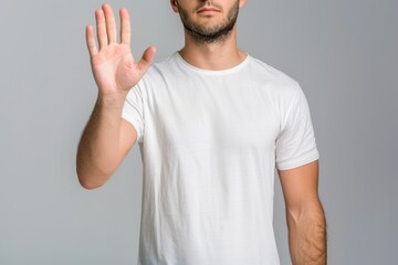 Naklejka premium Man standing in a white t-shirt raising his hand in a stop gesture in a neutral background setting