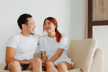 Asian Thai couple chitchat and hugging, love marriage, living together, sitting on sofa in room house.
