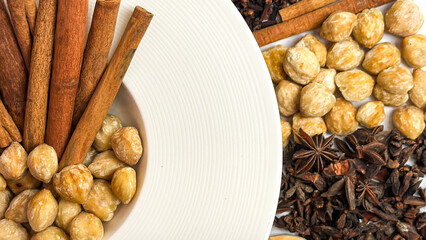 Top view of assorted traditional spices used in Indonesian and Asian cooking,including ginger, turmeric,galangal, cinnamon sticks, cloves, coriander seeds, and candlenuts on white background.