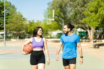 Cheerful Latin couple walking and talking on outdoor basketball court