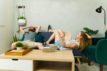 Couple sitting on sofa at home and suffering from the heat during summer heat wave
