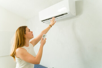 Young woman adjusting air conditioning temperature using remote control during summer heat