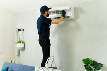 Male technician cleaning air conditioning unit with detergent and sponge