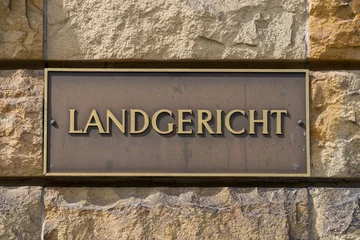 German courthouse signage on brass plaque. The word “Landgericht” engraved on a golden sign mounted on a coarse stone wall. © CC-IMAGES