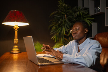 Professional black woman experiencing wrist discomfort from extended laptop use, rubbing sore hand...