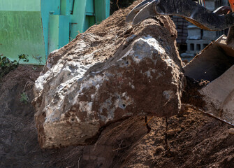 Heavy construction machine, equipped with a claw attachment, lifts a large, irregularly shaped hunk...