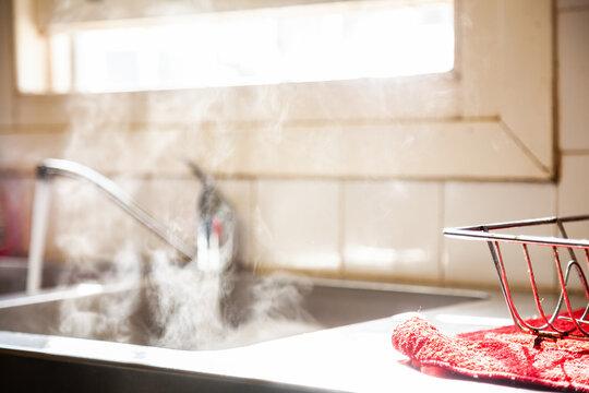 Steam from hot washing up water running into kitchen sink from tap