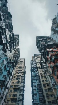 View looking up at stacked colorful apartment buildings with many windows and air conditioners in an urban area against an overcast sky.
