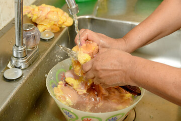 Woman washes raw chicken under running water in the sink. Food preparation at home. Washing raw chicken in the sink.