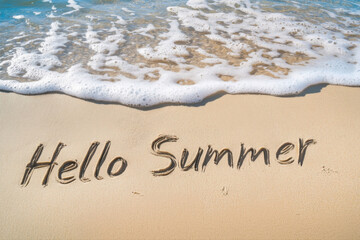 Text "Hello Summer" written in beach sand with ocean waves.
