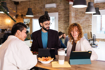 Coworkers discussing work during breaktime with digital tablets and snacks