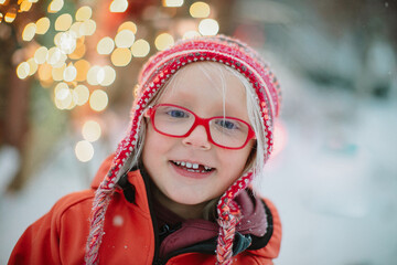 a portrait of a smiling little blond girl with the red glasses and a red hat