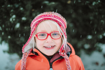 a portrait of a smiling little blond girl with the red glasses and a red hat