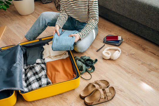 Young female traveler sitting on floor packing suitcase preparing for summer vacation trip