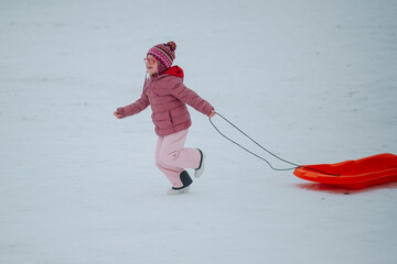 girl in a pink snowsuit running with the sled on a snowy hill