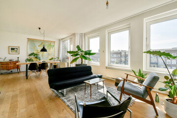 A spacious living room featuring a stylish black sofa, large windows, a vintage map, and contemporary furnishings, creating a relaxing and inviting atmosphere.