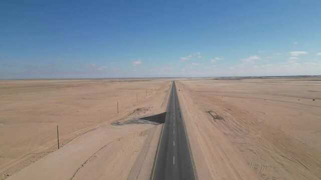 Drone footage of a long road in a vast desert landscape under sunlight and blue sky in Namibia