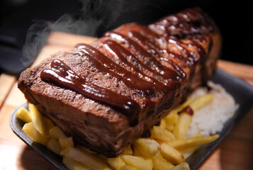 Ribs with barbecue sauce accompanied by a portion of fries and rice. Light worked with a close view.
