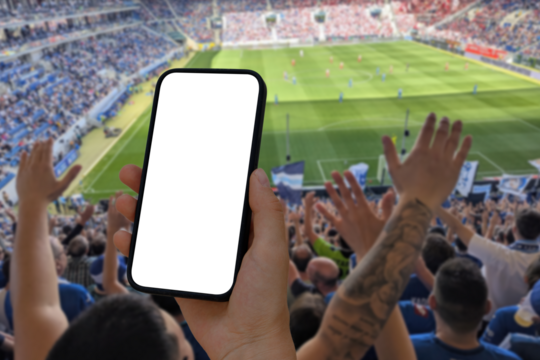 Cell phone with transparent screen in human hands. In the background, out of focus, a football stadium with cheering fans. 