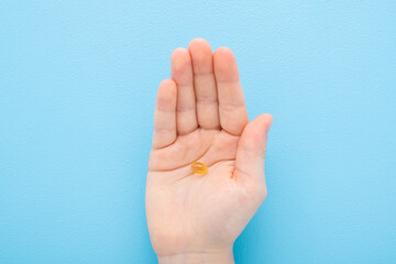 Little child boy palm holding and showing fish oil capsule or d vitamin on light blue table...