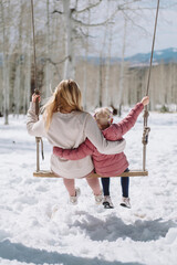 mother and daughter on a swing in a the snowy mountains