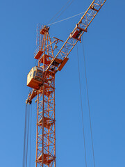 Fototapeta premium Equipment for the construction and lifting of bulky goods with construction materials. A tower crane on a construction site against a blue sky background. Construction equipment.