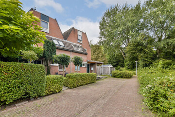 A captivating view of a brick house surrounded by lush greenery and well-maintained hedges, complemented by a serene pathway leading to the entrance.