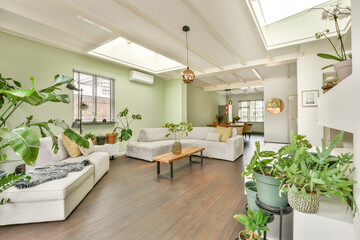 A stylish modern living room featuring comfortable seating, natural light, and an abundance of indoor plants, creating a welcoming atmosphere.