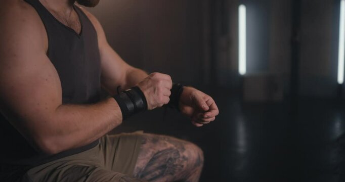 Close-up of a strong man adjusting wrist wraps in a moody gym setting