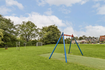 Fototapeta premium A lively playground featuring colorful swings, lush green grass, and trees creating an inviting environment for play and relaxation.