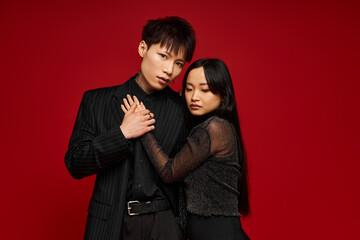 Stylish couple expressing love against a vibrant red backdrop in a dynamic fashion shoot