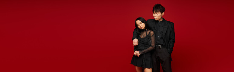 Stylish couple dressed in black poses against a vibrant red backdrop expressing love and romance