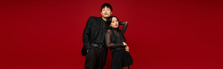 Stylish couple poses against vibrant red backdrop radiating love and fashionable charm