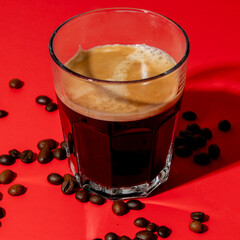 Fresh espresso in a glass with scattered coffee beans on red background, perfect for morning energy...