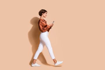 Full length photo of good mood cute lady dressed silky shirt walking chatting modern device walking...