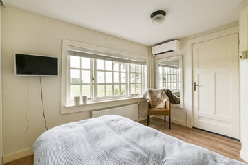 A serene bedroom featuring soft bedding, a comfortable chair, and a large window that lets in natural light. Neutral tones create a calming atmosphere.