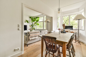 A stylish modern living space featuring a wooden table, comfortable seating, and abundant natural light from large windows, complemented by indoor plants.