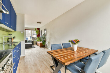 A stylish kitchen and dining area with blue cabinets, wooden table, and decorative plants creating a cozy atmosphere, ideal for mealtime gatherings and relaxation.
