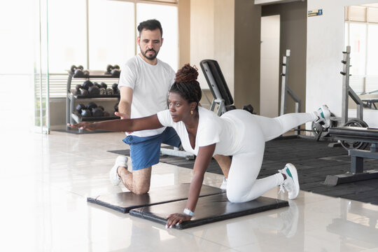 Personal trainer guiding client doing bird-dog exercise in gym
