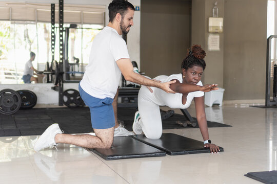 Personal trainer assisting client doing bird-dog exercise in gym