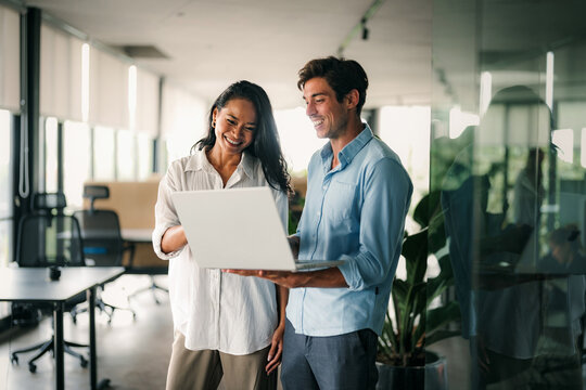 Diverse team of two business people working talking using tablet tech walking in corporate office. - Powered by Adobe