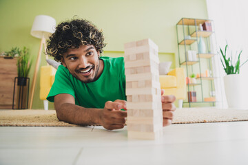 Fototapeta premium Portrait of nice young man play jenga blocks game floor wear t-shirt modern green interior flat indoors