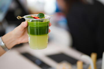 Close up and selective focus hand of woman holding a take-out iced match lemon with herb at cafe