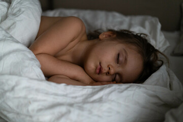Cute toddler boy sleeps on white bed linen.The face looks at the camera.