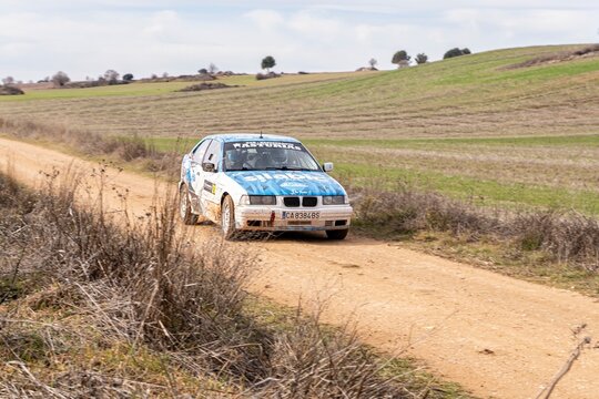 Madrid, Spain; 02-15-2025: A blue and white BMW 323i E36 navigates a gravel rally track, kicking up dust as it speeds through the countryside